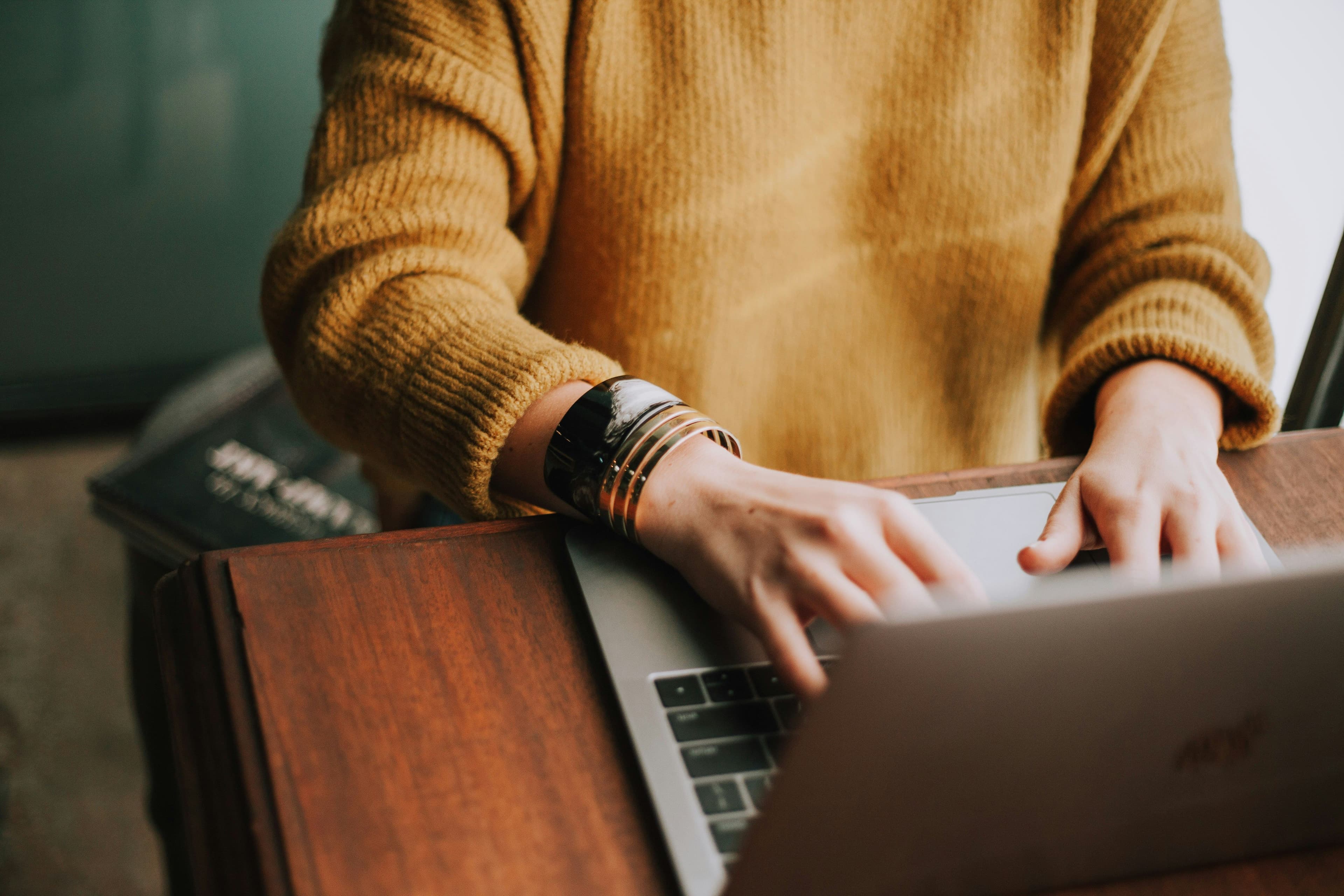 Person in cozy sweater working on laptop, representing human-centered technology
